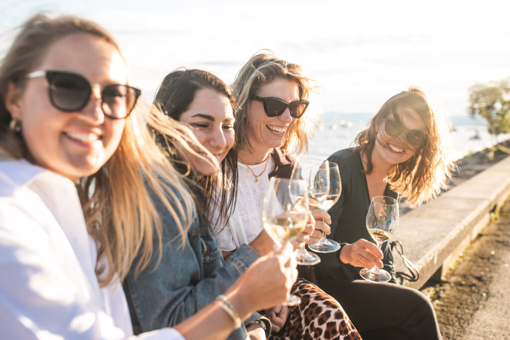 Un groupe de femmes assises sur un muret rie et boit du vin blanc