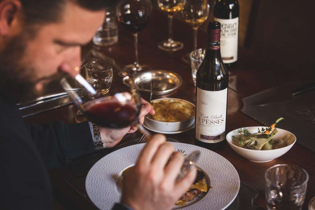 Un homme sent un vin rouge, devant une table de mets